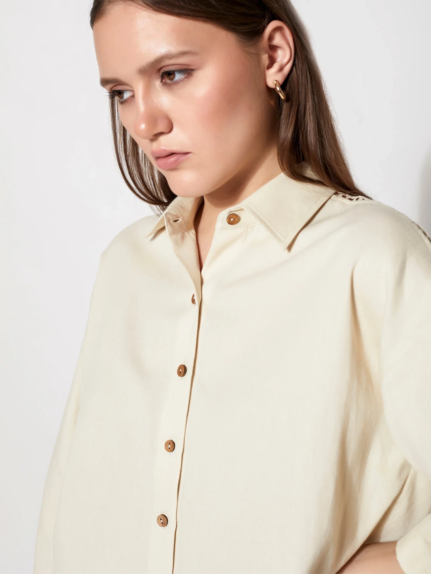 Woman wearing a cream button-up shirt with wooden buttons, minimal luxury fashion style