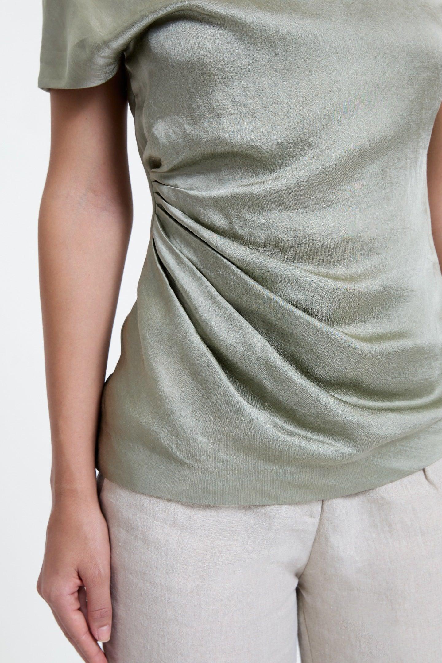 Close-up of sage green ruched women’s top with short sleeves and light beige pants