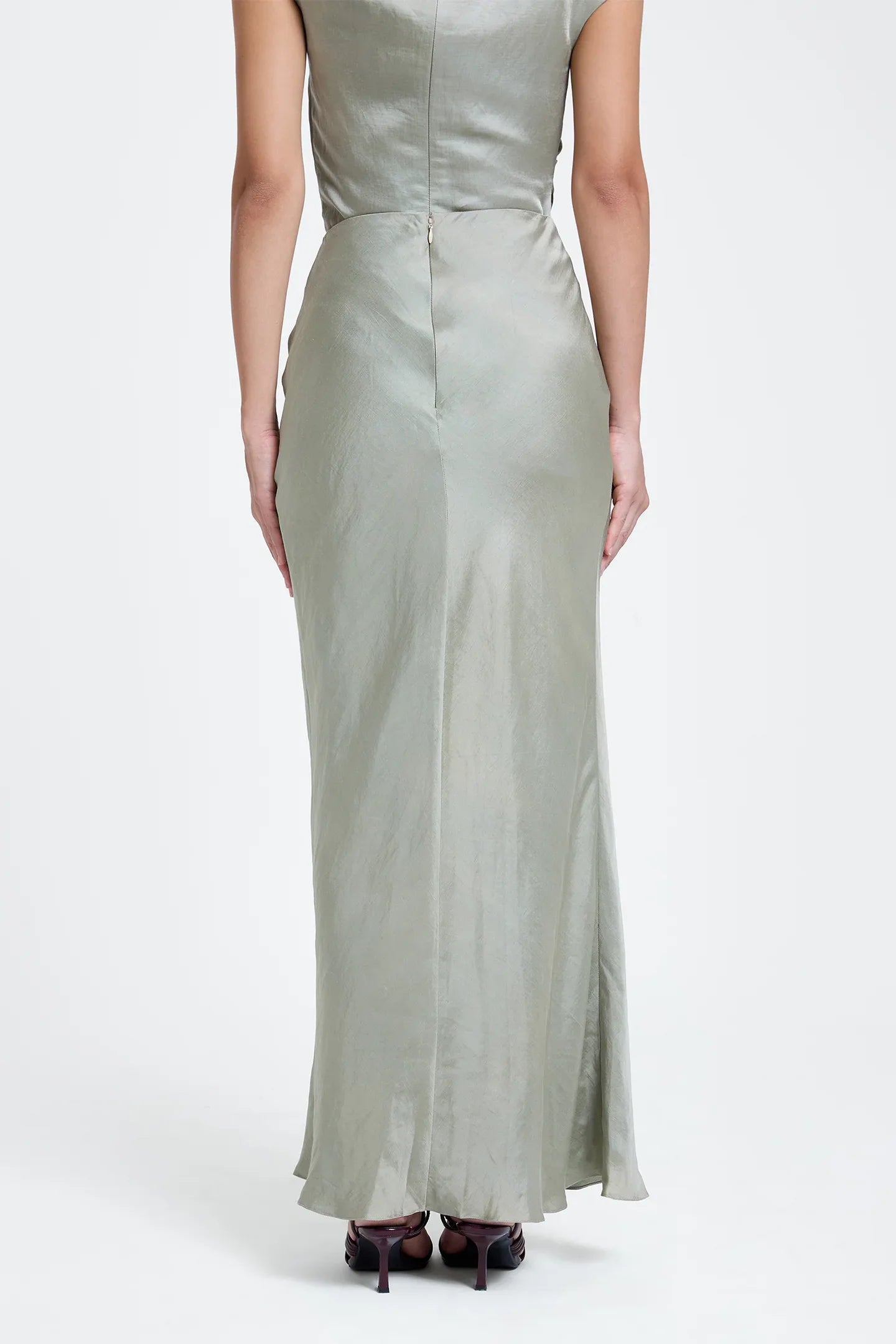 Woman in a sage green, off-shoulder satin top and maxi skirt, standing against white background