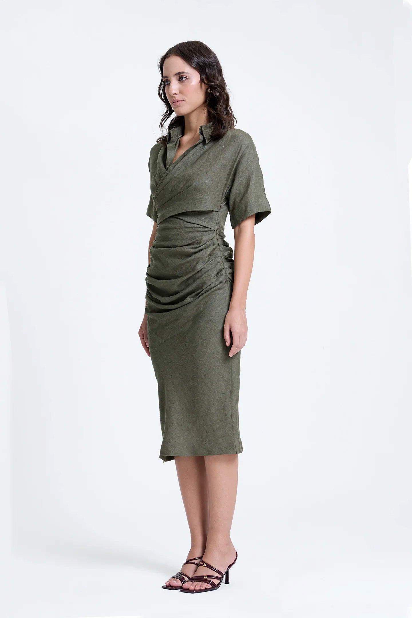 Woman wearing olive green ruched midi dress with short sleeves and v-neck, standing