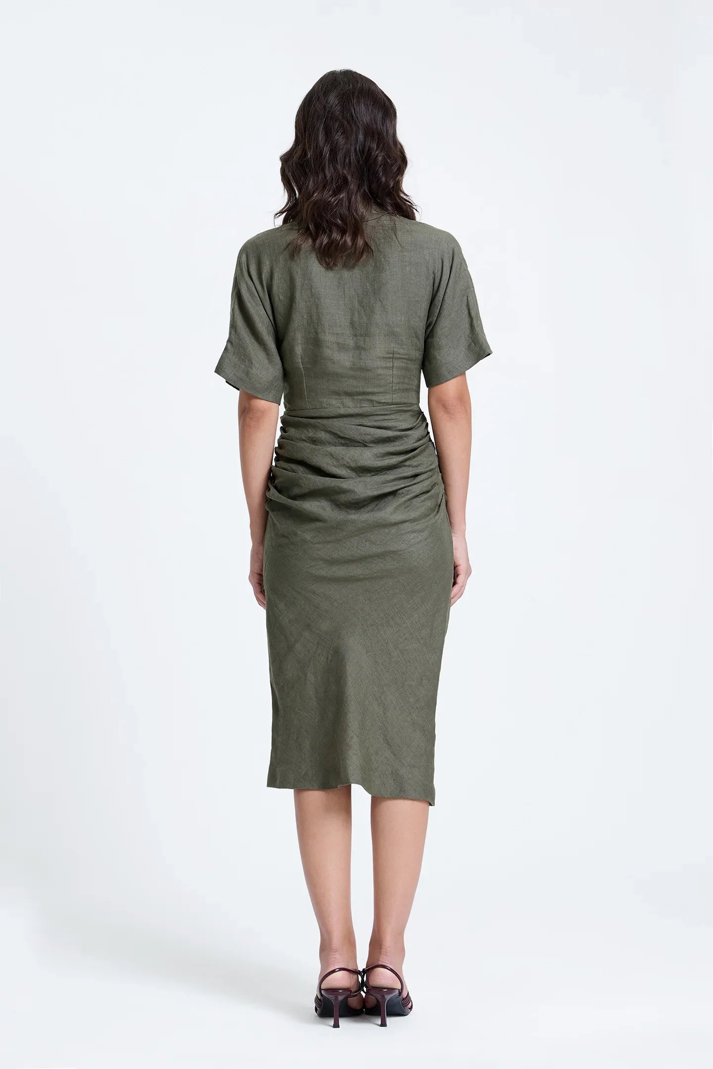 Back view of woman in olive green ruched midi dress with short sleeves and heels