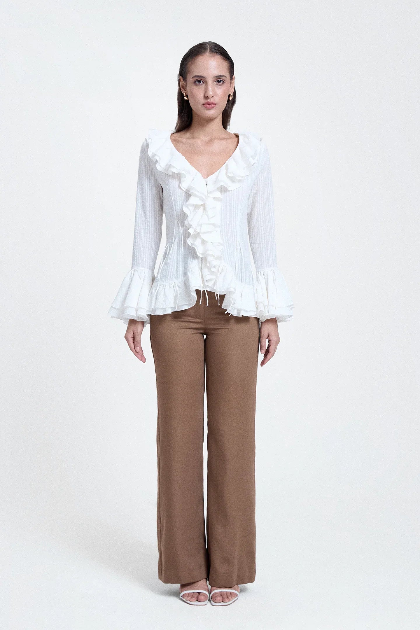 Woman wearing a white V-neck ruffled top with long sleeves and brown wide-leg pants
