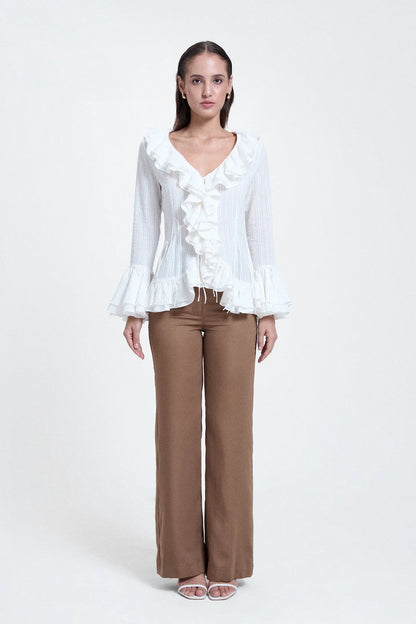 Woman wearing a white V-neck ruffled top with long sleeves and brown wide-leg pants